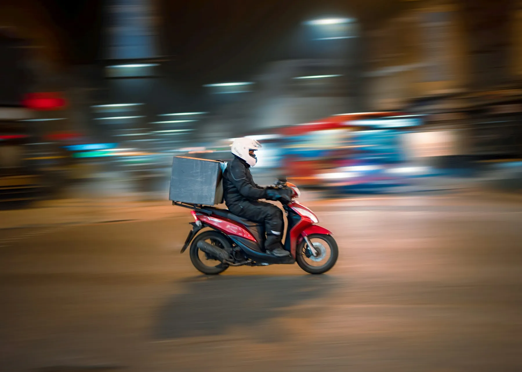 A delivery rider on a scooter in city traffic.